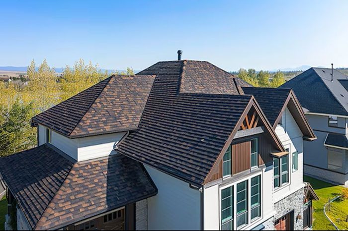 Brown shingled roof of a two-story house with white siding and a mountain backdrop.