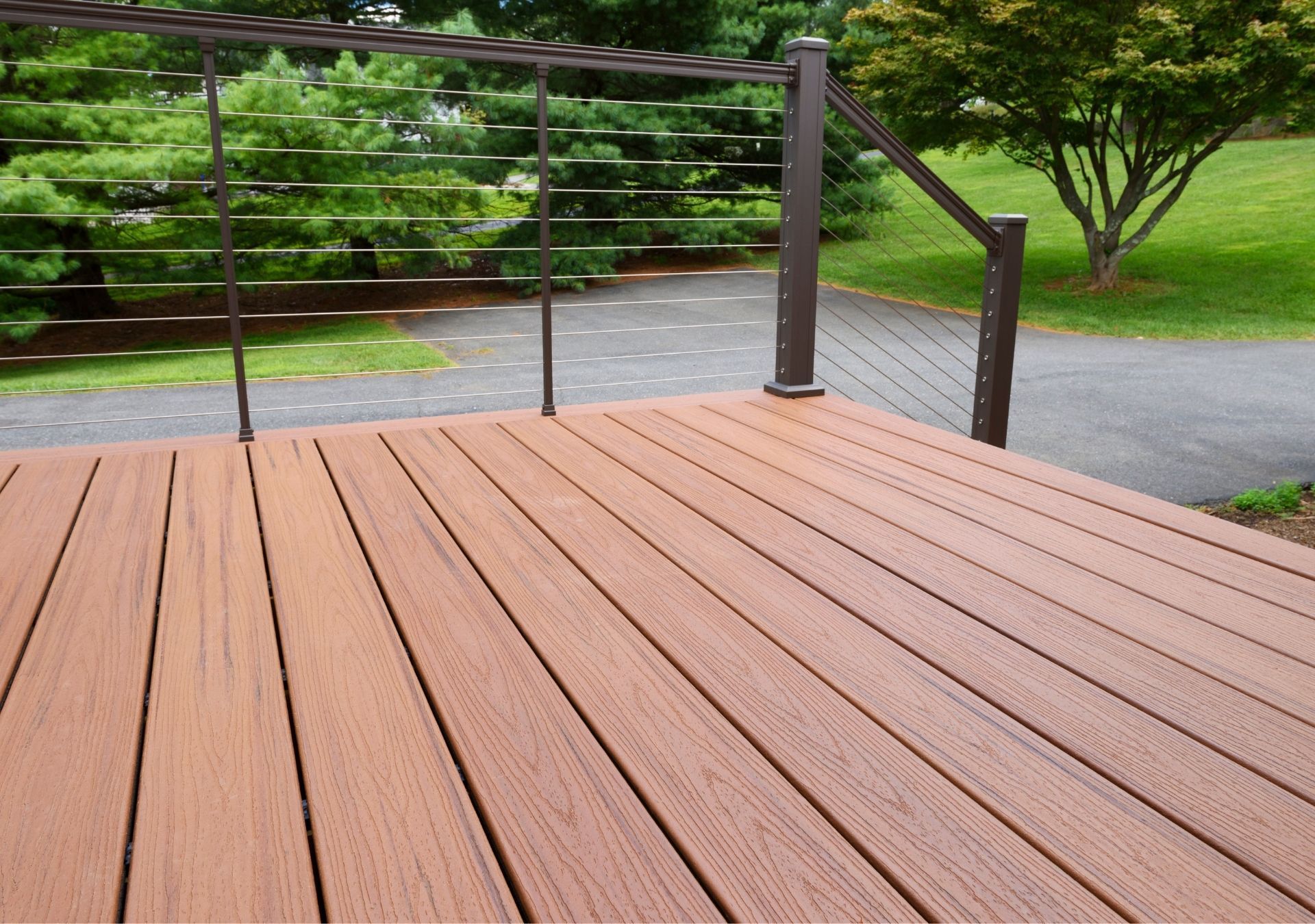 Wooden deck with metal railing overlooking a driveway and green yard.