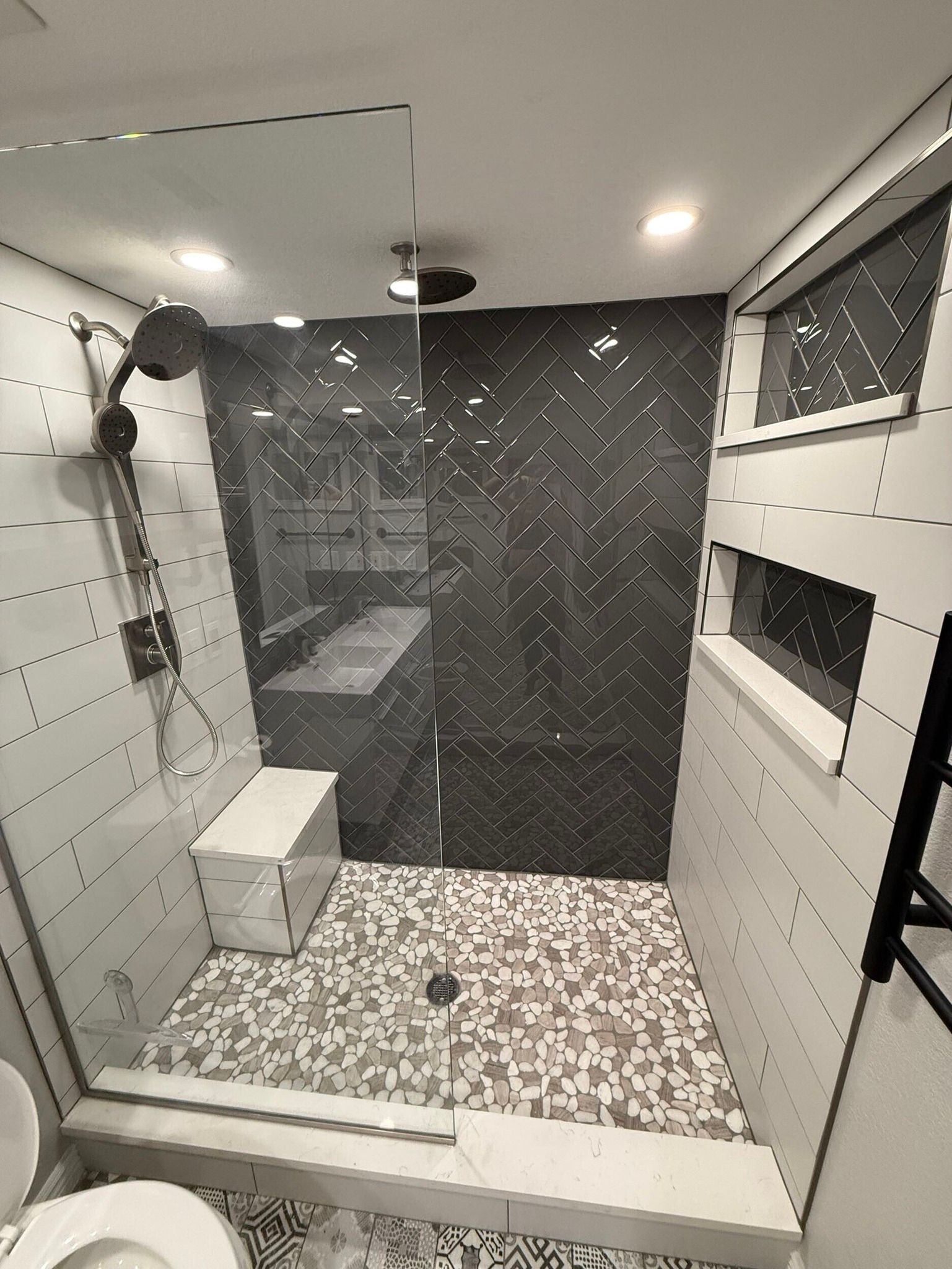 Modern bathroom with glass shower, dark herringbone tile, mosaic floor, and white walls.