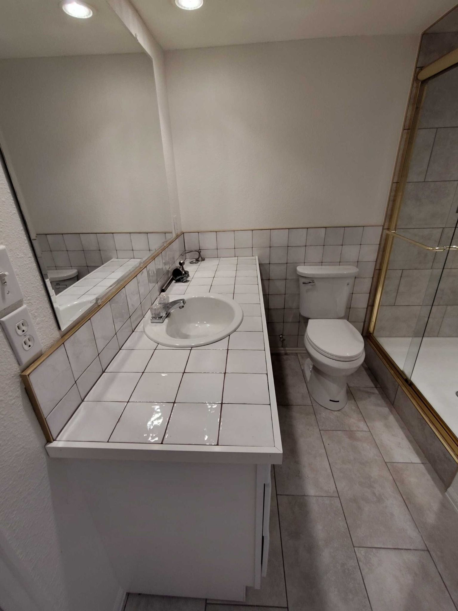 Bathroom with white tile, vanity, toilet, mirror, and glass shower door.