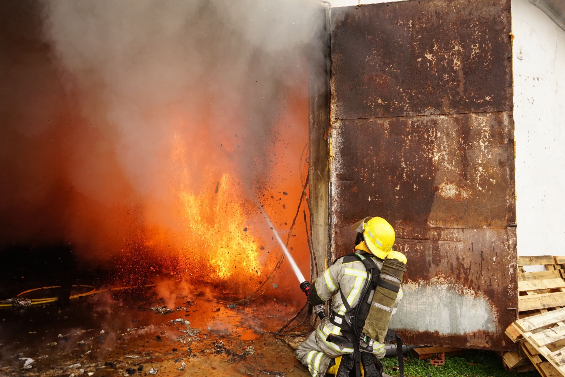 Firefighter spraying water on a building engulfed in flames.