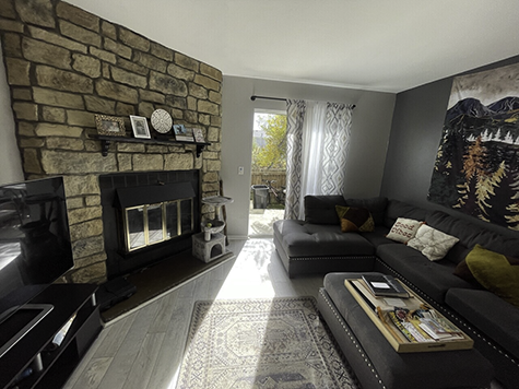 Living room with stone fireplace, gray sectional sofa, and rug. Sliding door to outside.
