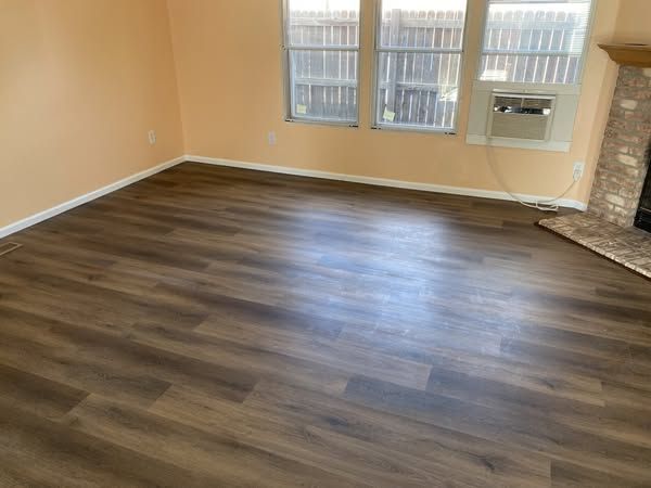 Empty living room with brown wood-look flooring, peach walls, and a window with an AC unit.