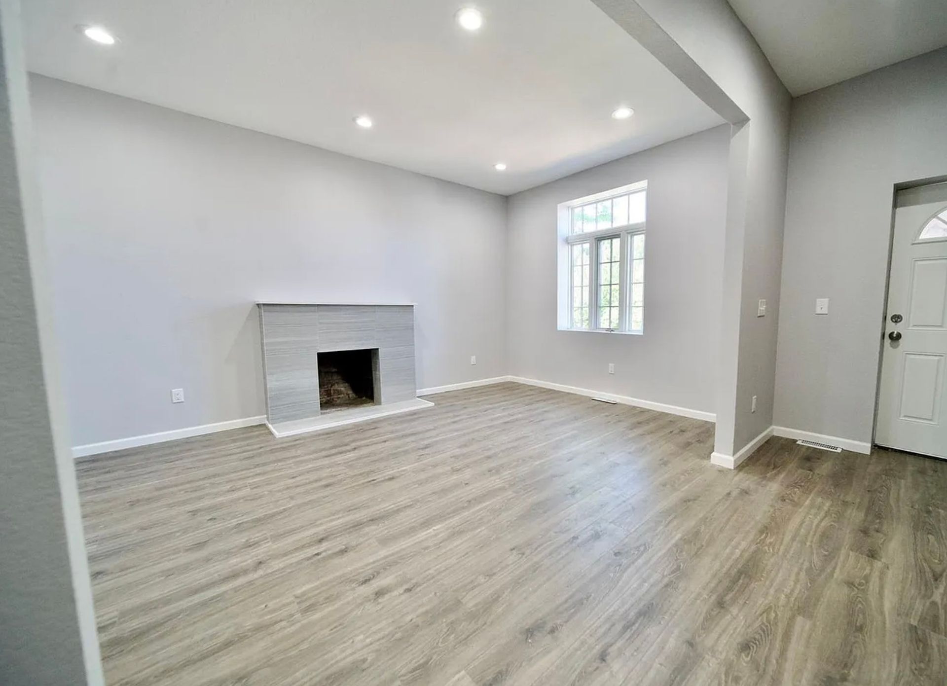 Empty living room with gray walls, a fireplace, and a window. Light wood-look flooring.