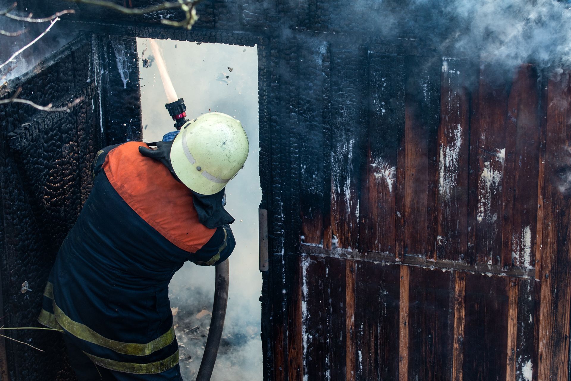 Firefighter sprays water into a burning wooden structure.