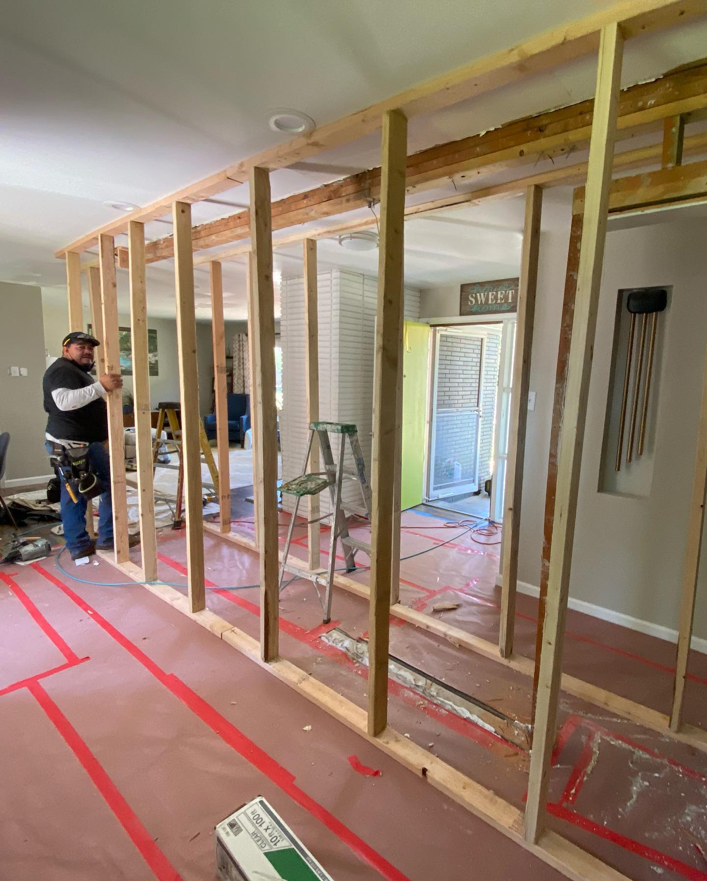 Man constructing wooden wall frame in room with pink insulation on floor.