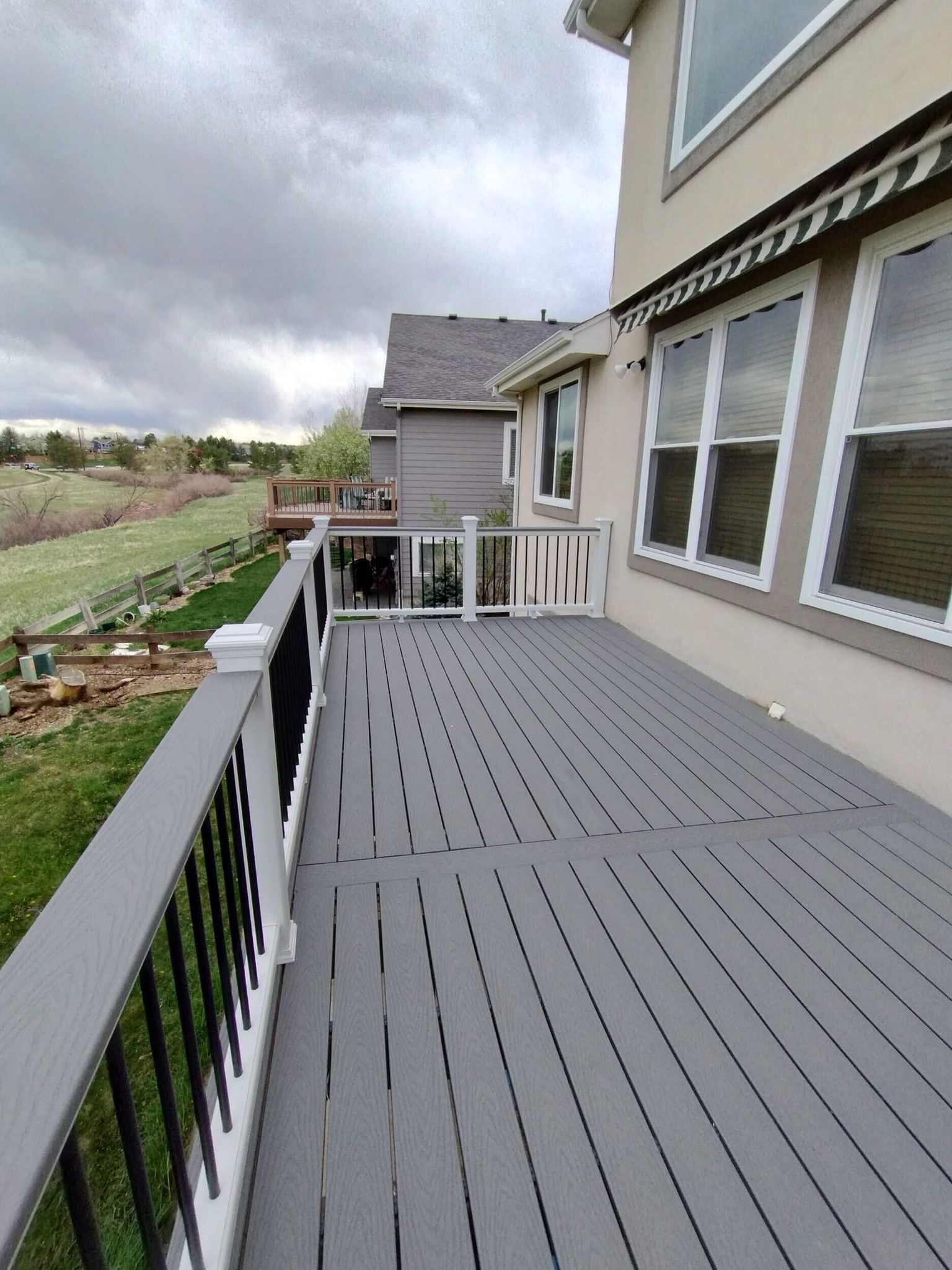 Gray composite deck with black railing next to a tan house. Overcast sky.