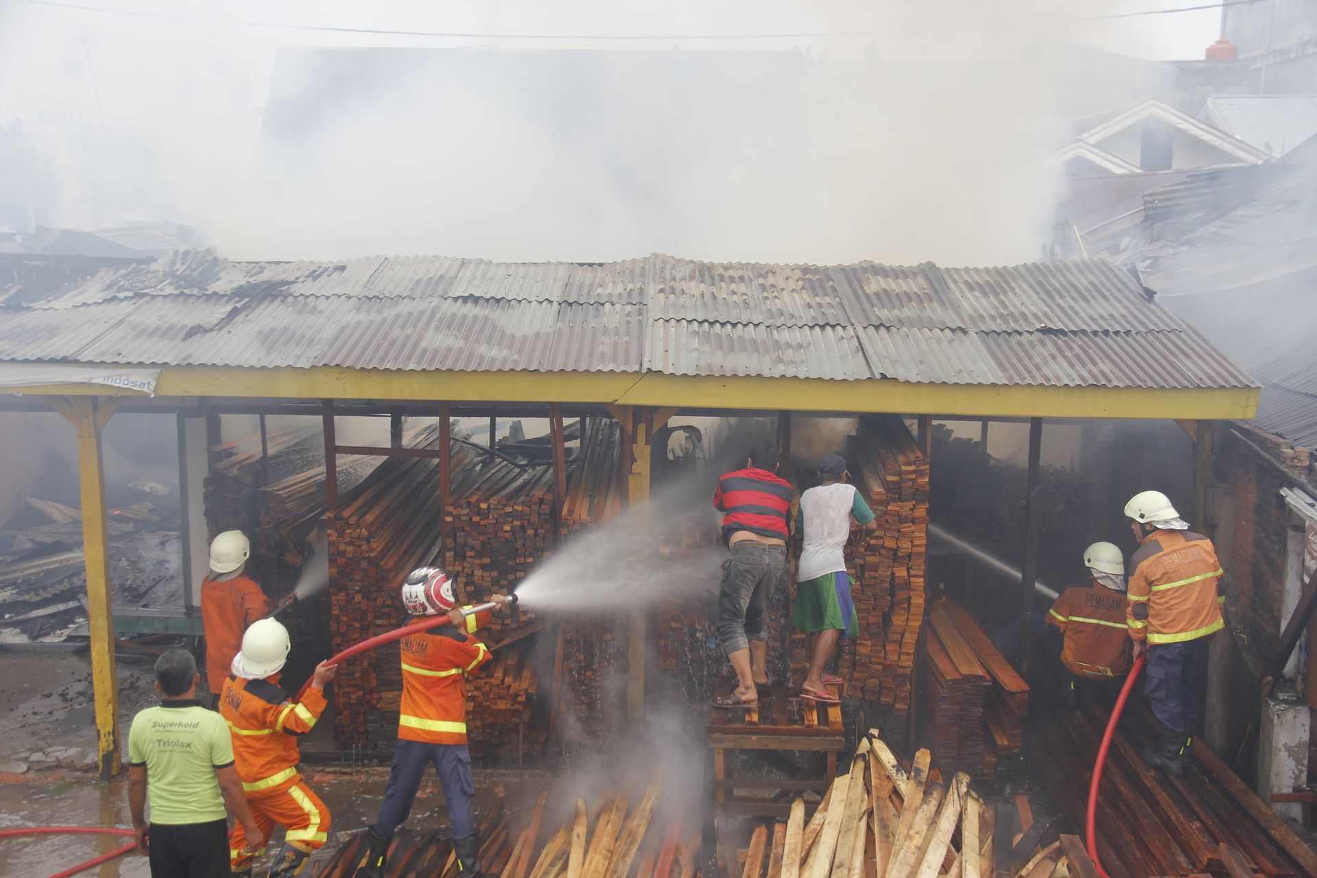 Firefighters in orange suits spraying water on a burning wooden structure, smoke billowing.