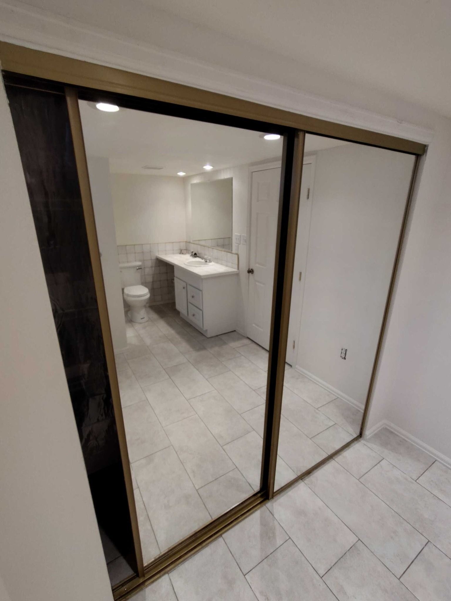 Mirrored closet doors reflect a white bathroom with a double sink vanity and toilet.