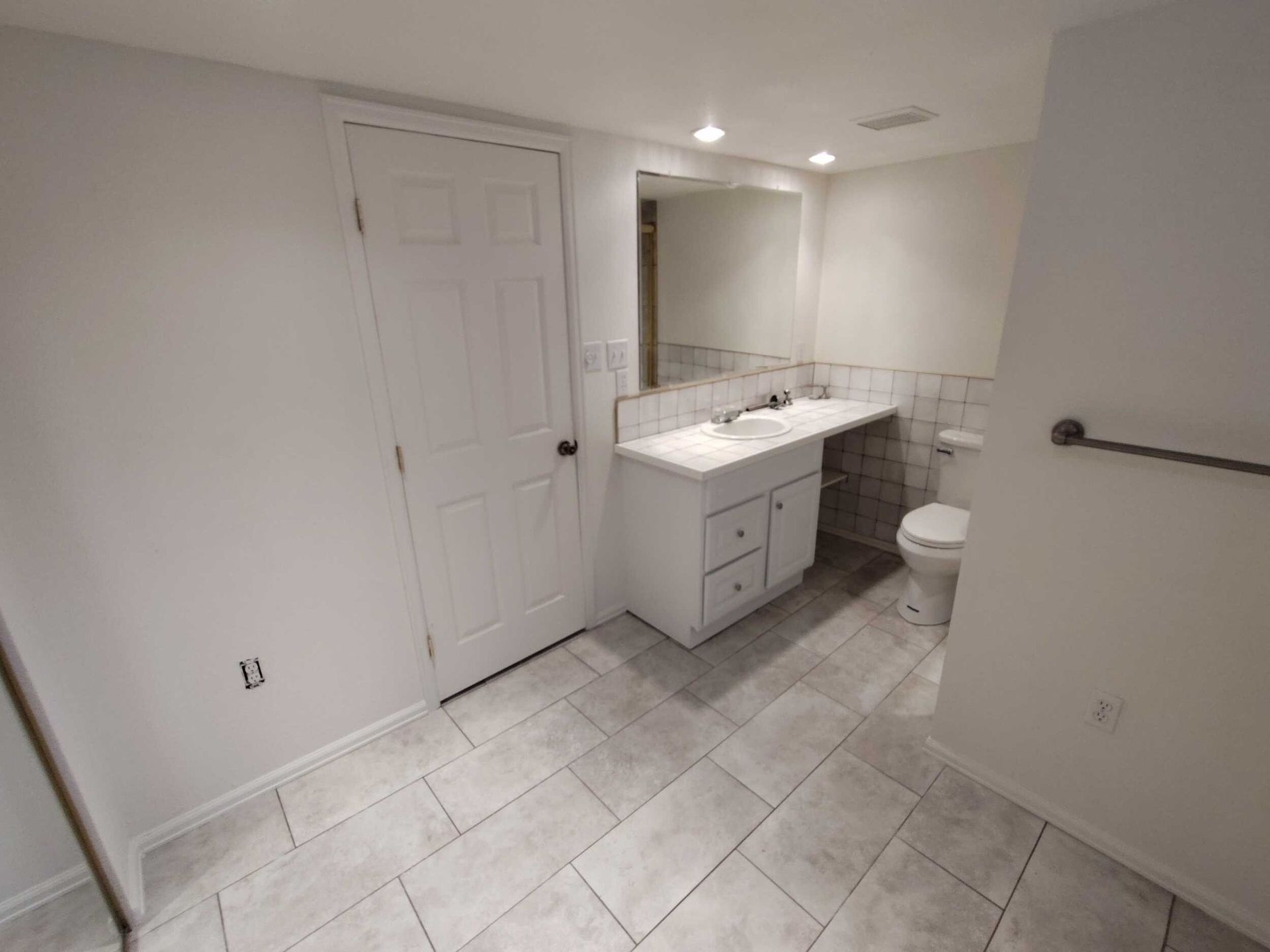 Bathroom with white walls, vanity, toilet, and tiled floor.