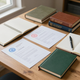 Notebooks and stamped documents arranged on a wooden desk near a window.