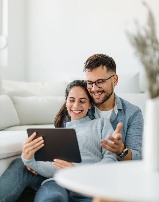 A man and a woman are sitting on a couch looking at a tablet.