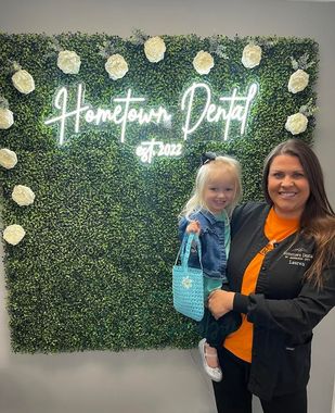 Woman in scrubs holds a smiling child in front of a wall with a 