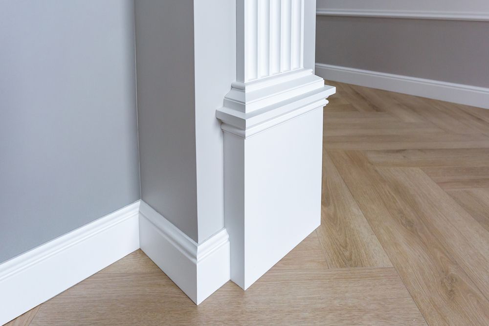 Corner of a room with white trim, a fluted column, and wood floor, with gray and white walls.
