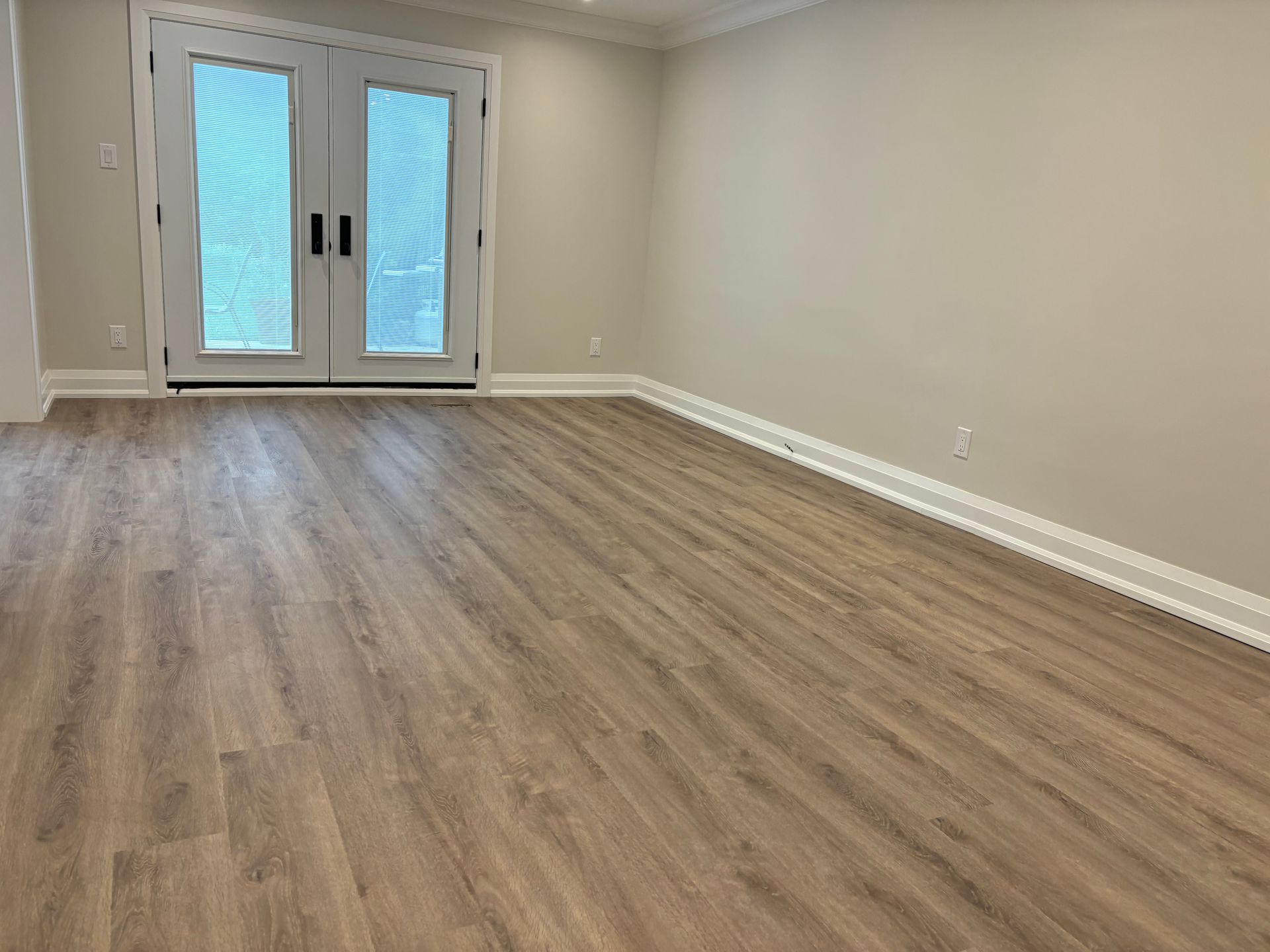 An empty living room with hardwood floors and french doors.