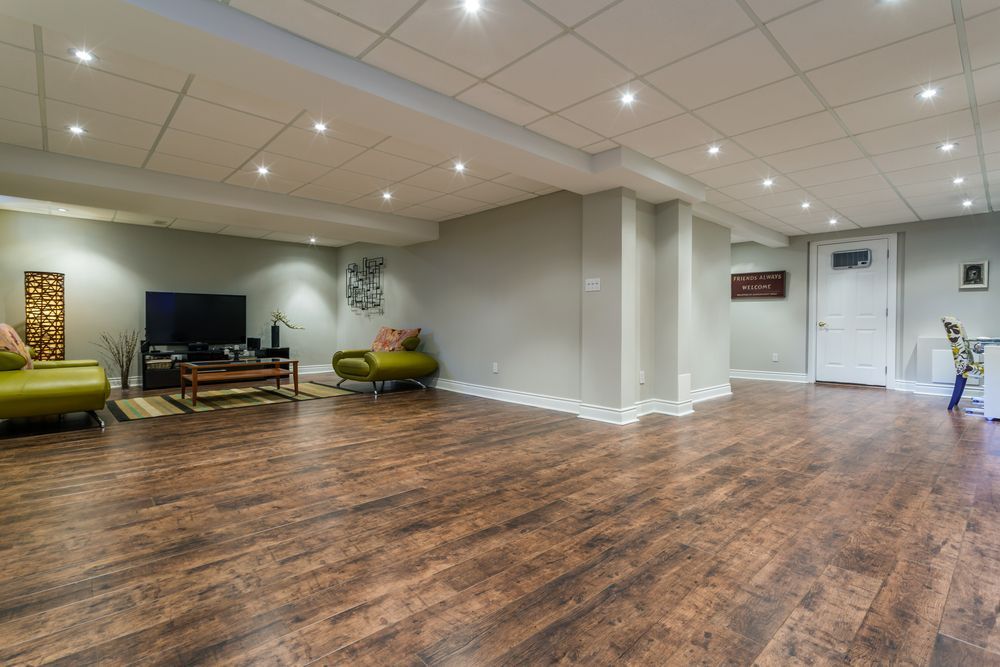 Spacious basement with wood-look floor, olive furniture, and TV; white ceiling and trim, neutral walls.