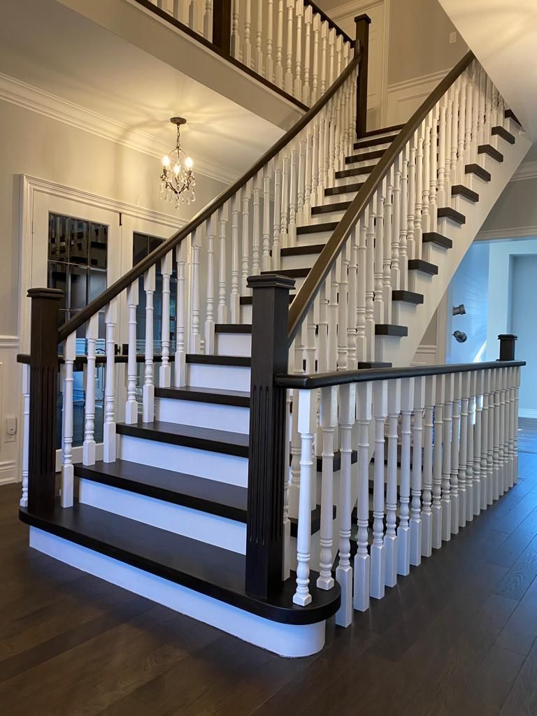 Elegant two-story staircase with dark wood treads, white balusters, and dark wood handrails in a light-colored home.