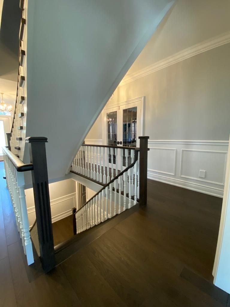 Dark wooden staircase with white railings, leading to a second floor hallway with wainscoting.
