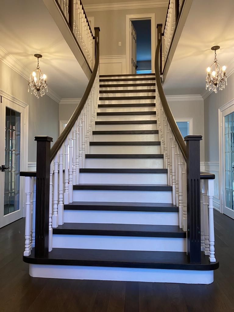 A grand staircase with dark treads and white risers, framed by a dark railing, lit by chandeliers.