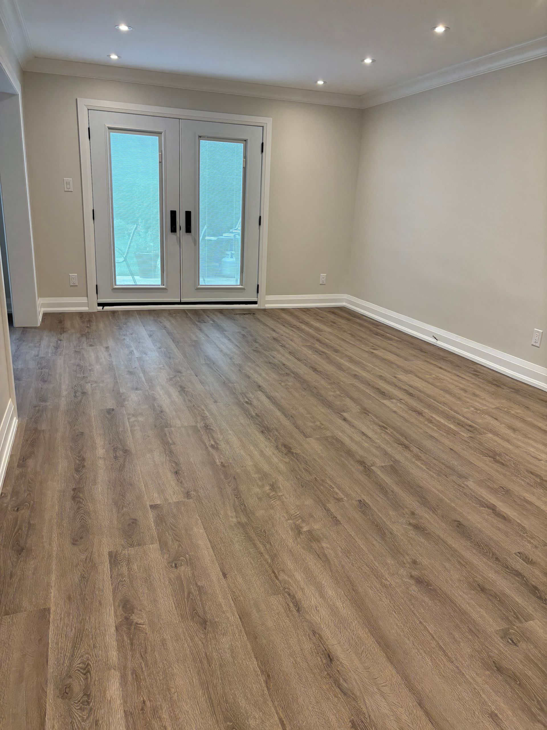 Empty room with wood-look flooring, beige walls, white trim, and French doors leading outside.