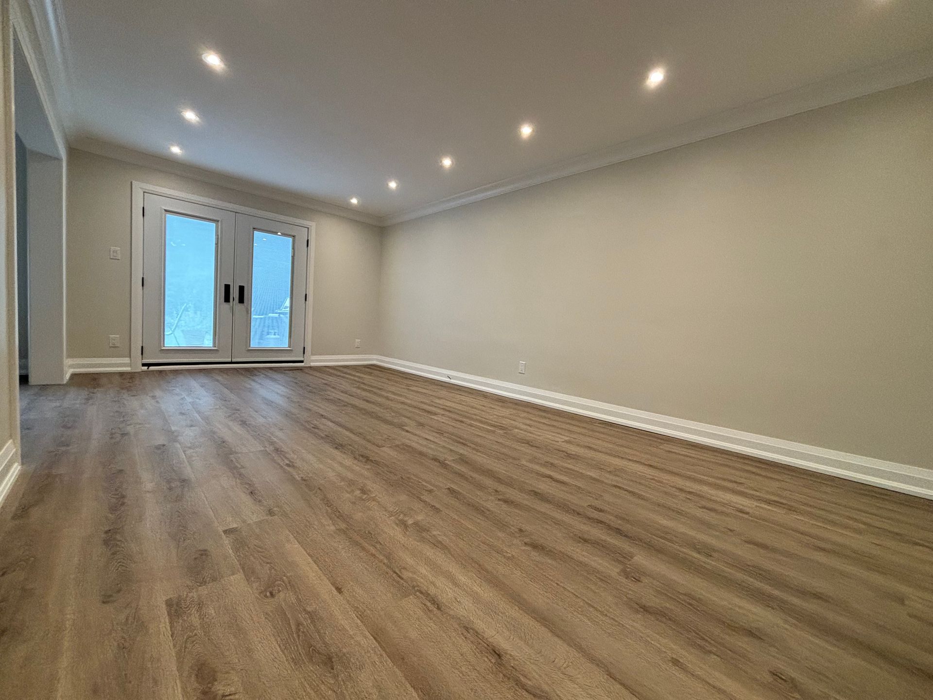 Empty room with hardwood floors, light walls, recessed lighting, and french doors.