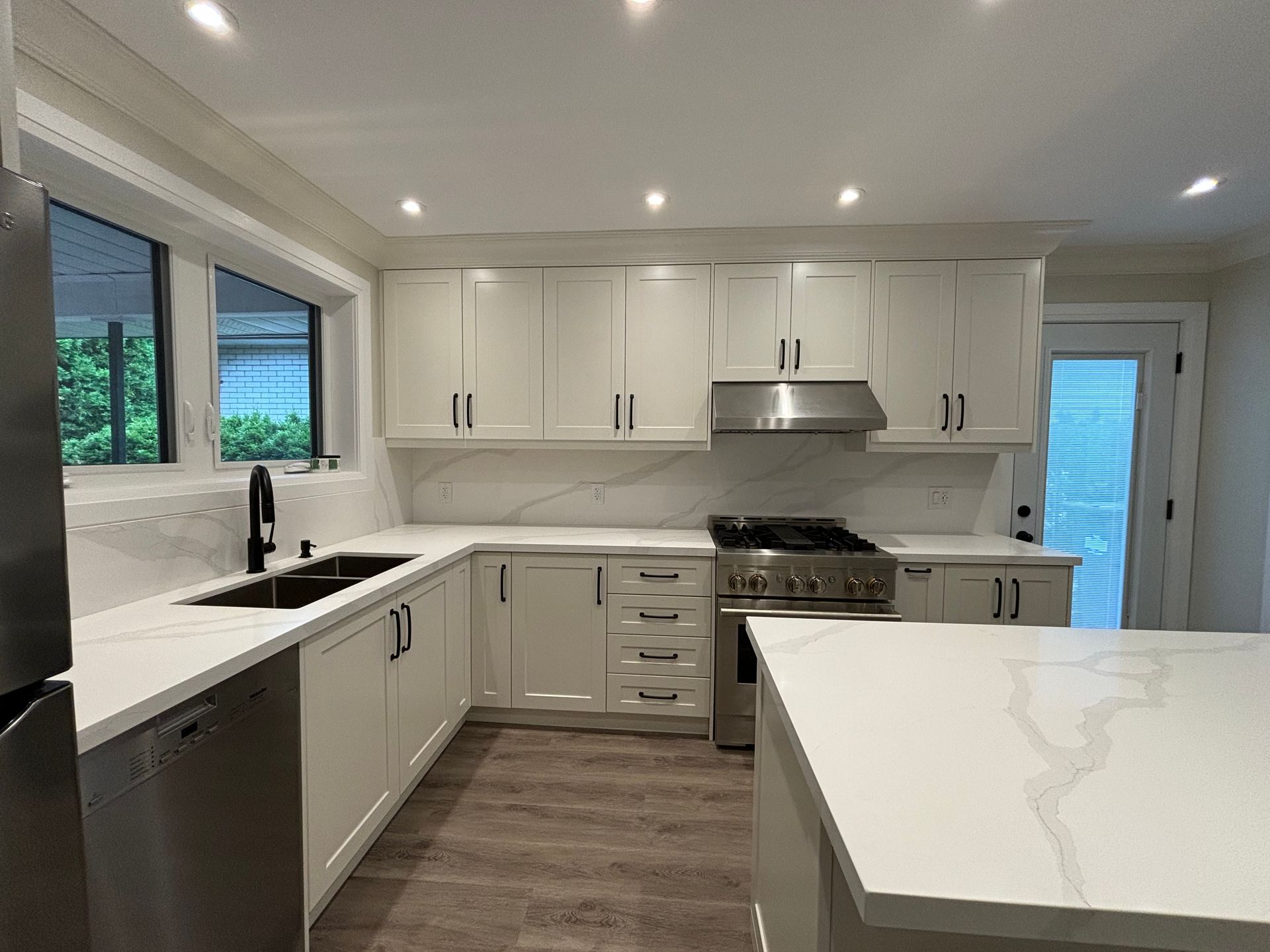 Modern kitchen with white cabinets, quartz countertops, stainless steel appliances, and dark hardware.