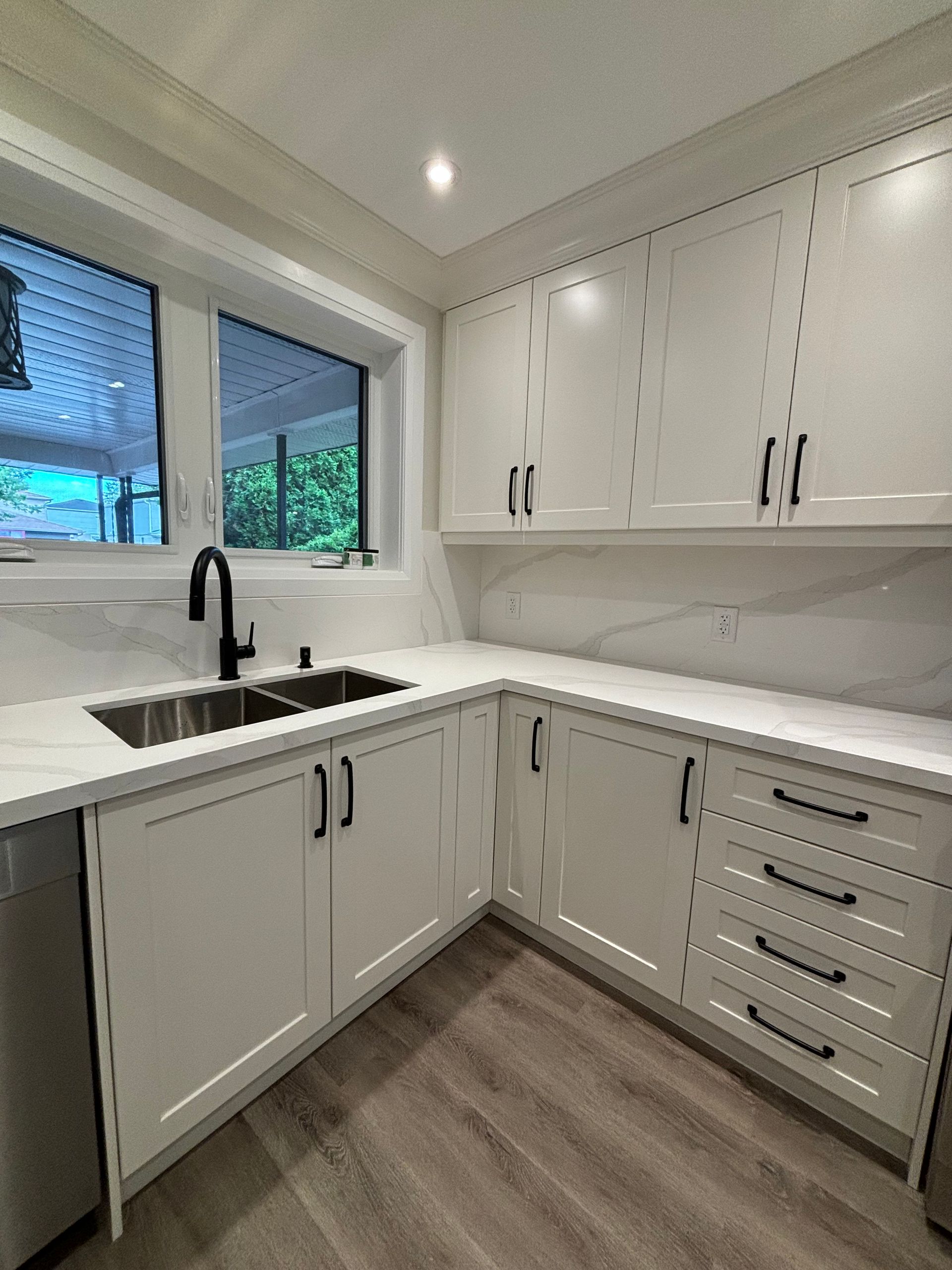 White kitchen with white cabinets, light countertop, dark faucet, and wood-look flooring.