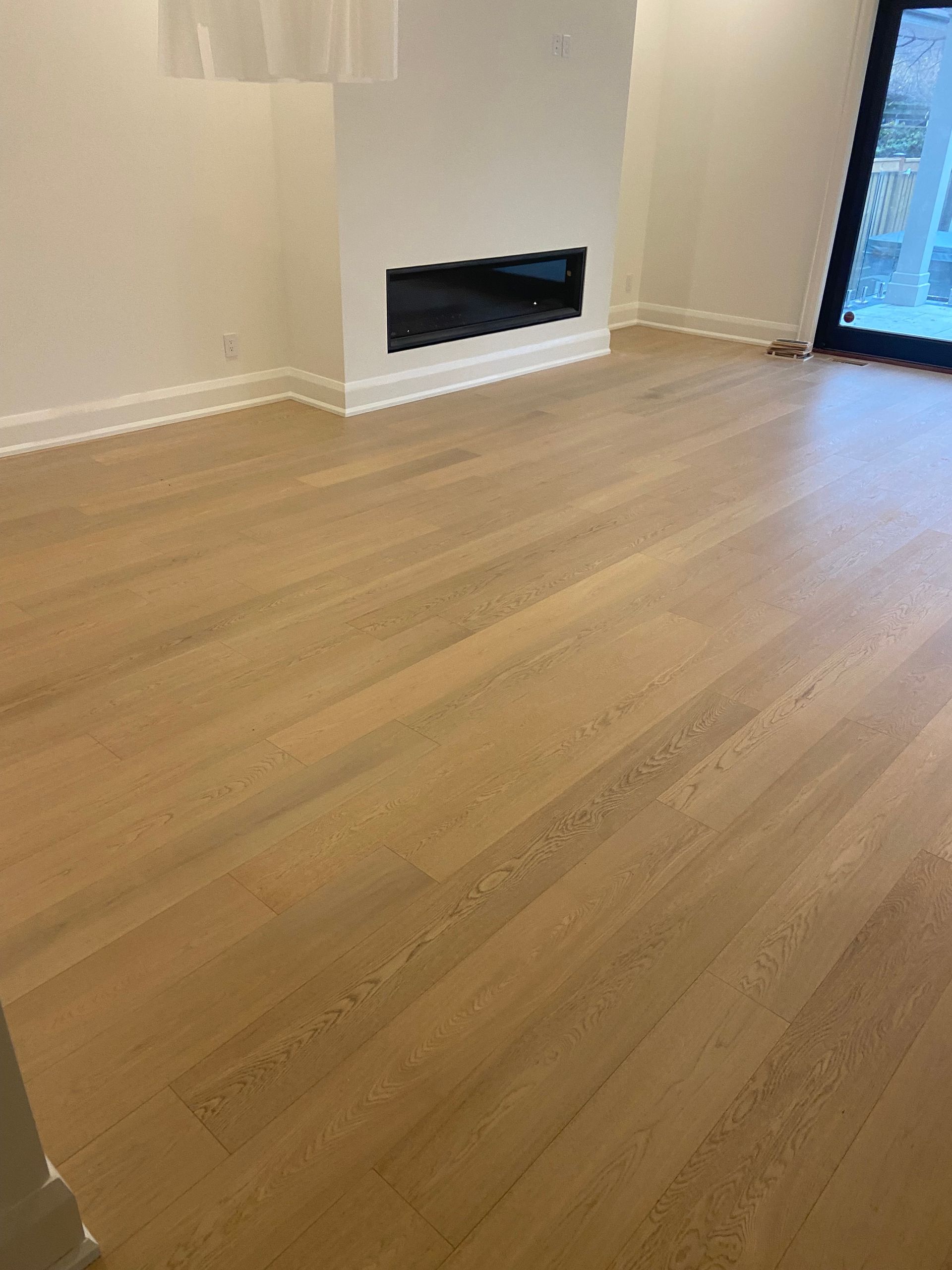 Light wood flooring in a room with a fireplace and large window.