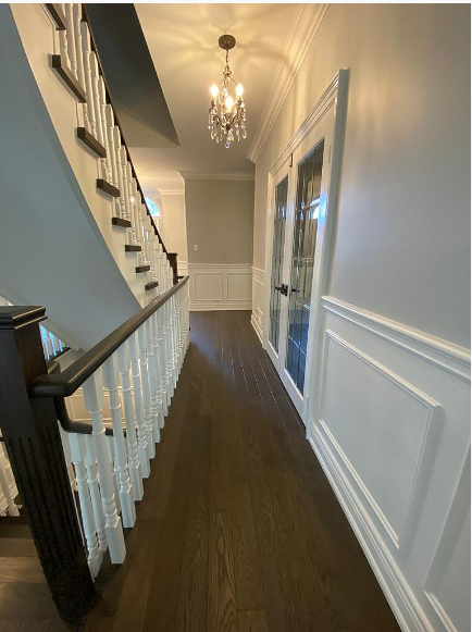 Hallway with dark wood floor, white wainscoting, and a staircase. A chandelier hangs from the ceiling.