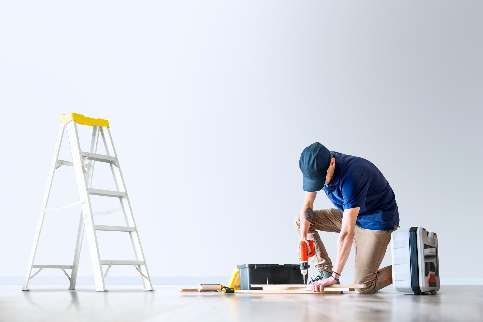 A man is kneeling on the floor using a drill.