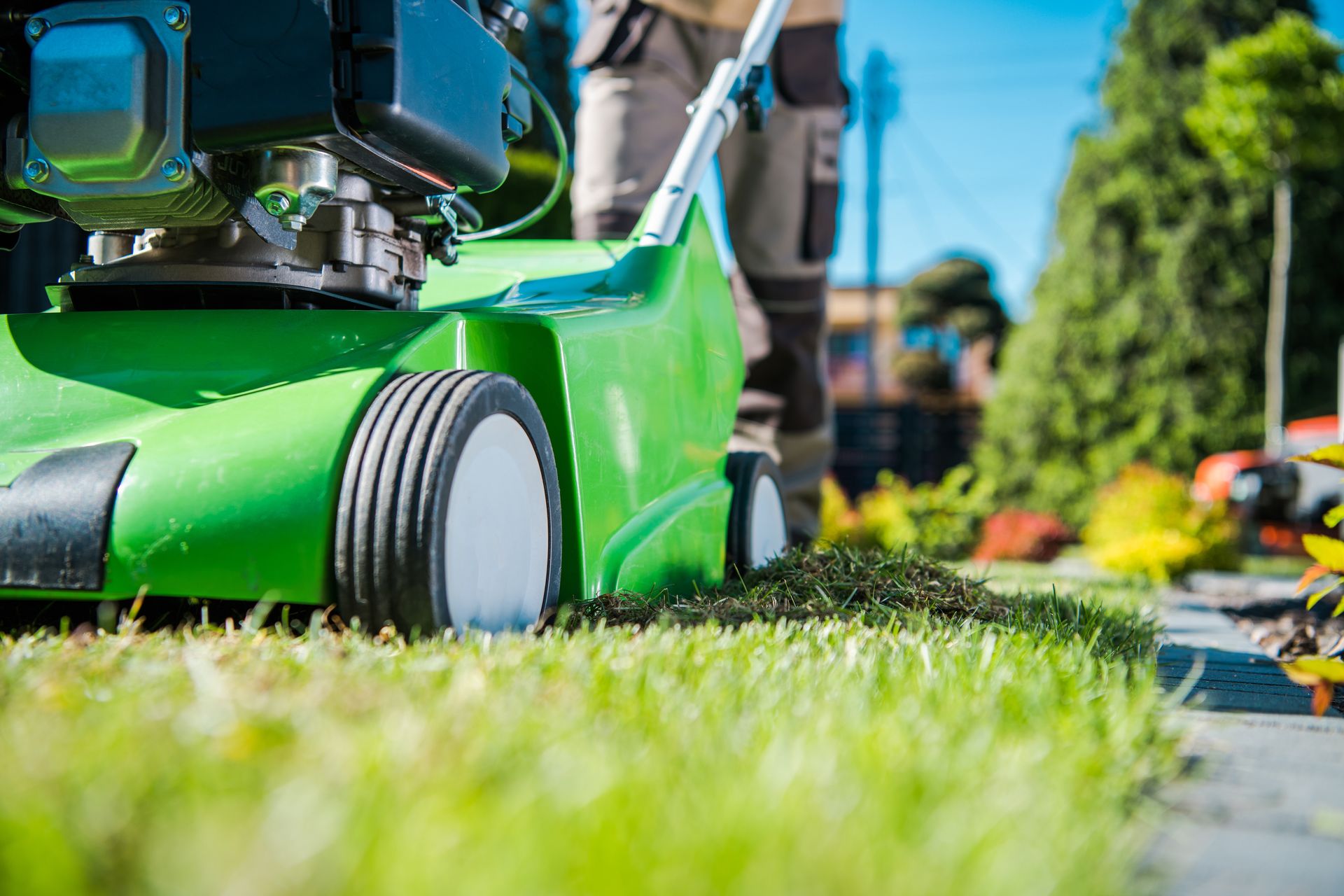 Green lawn mower cutting grass in a sunny garden with a blurred person in the background