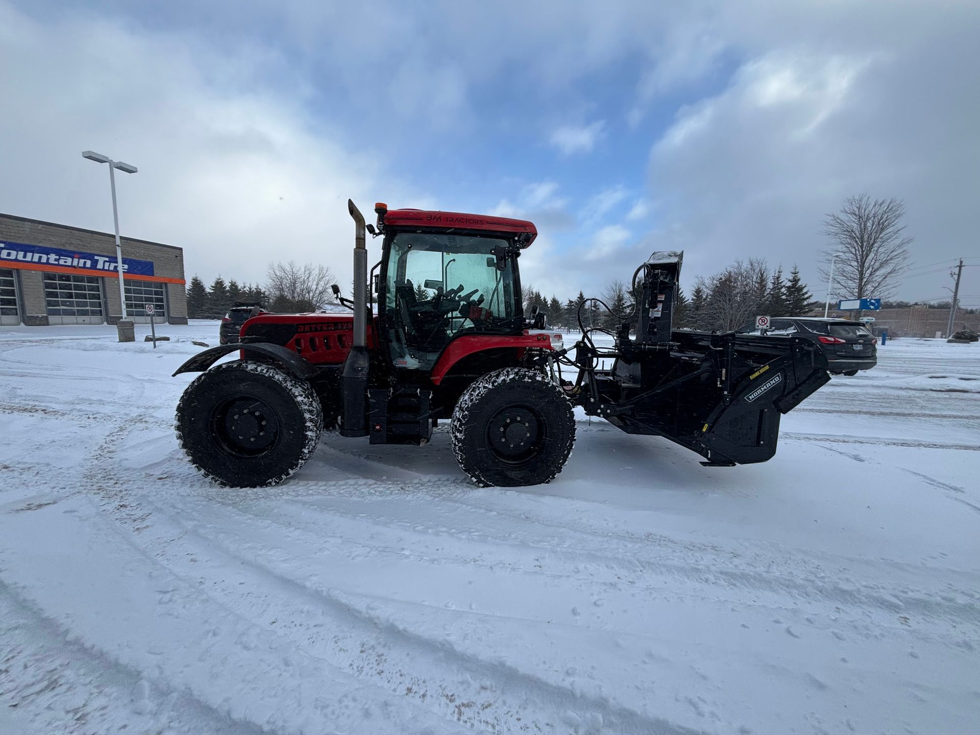 Red tractor with front loader parked on a snowy lot under a cloudy sky