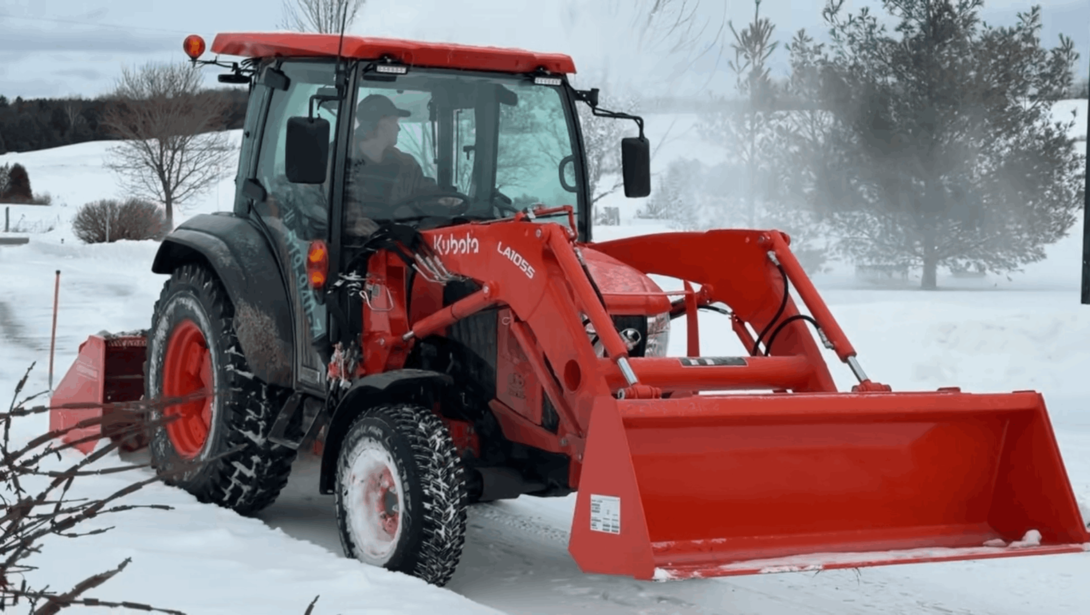 Red tractor with front loader clearing snow in a snowy field