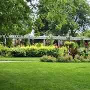 Lush green park lawn with colorful shrubs, white trellis, and large trees in the background