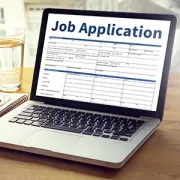 Laptop displaying a job application form on a desk beside a glass of water and notebook