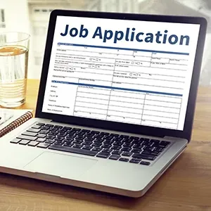 Laptop displaying a job application form on a desk beside a glass of water and notebook