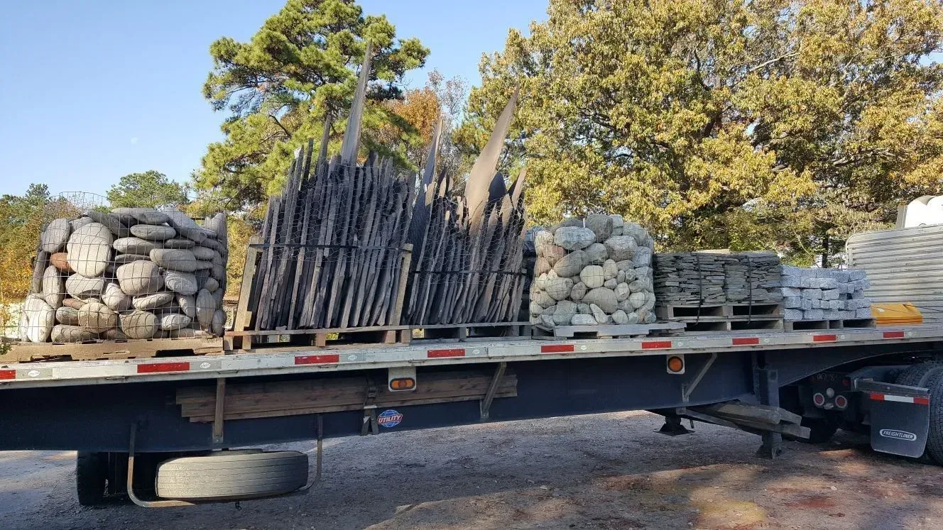 Flatbed truck loaded with stacked stone columns and rocks outdoors on a gravel lot