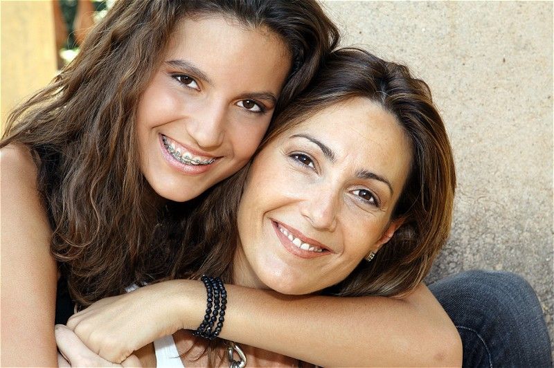 A mother and daughter are hugging each other and smiling for the camera.