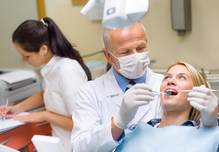A woman is sitting in a dental chair while a dentist examines her teeth.