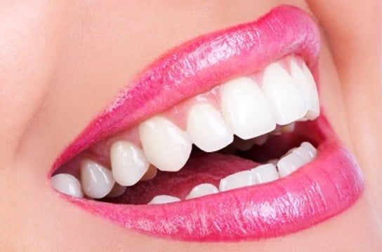 A close up of a woman 's mouth with white teeth and pink lipstick.