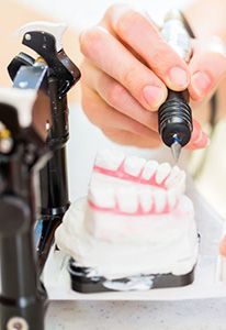 A person is holding a tool over a model of teeth.