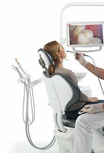 A woman is sitting in a dental chair being examined by a dentist
