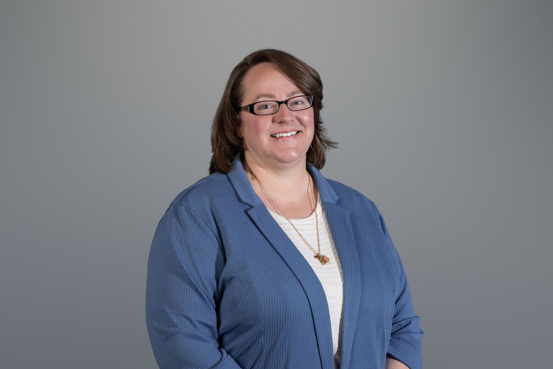 Woman in a blue blazer smiling against a gray studio background.