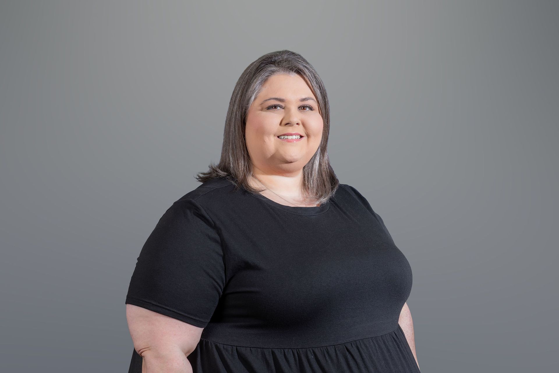Woman in a black dress smiling against a gray background