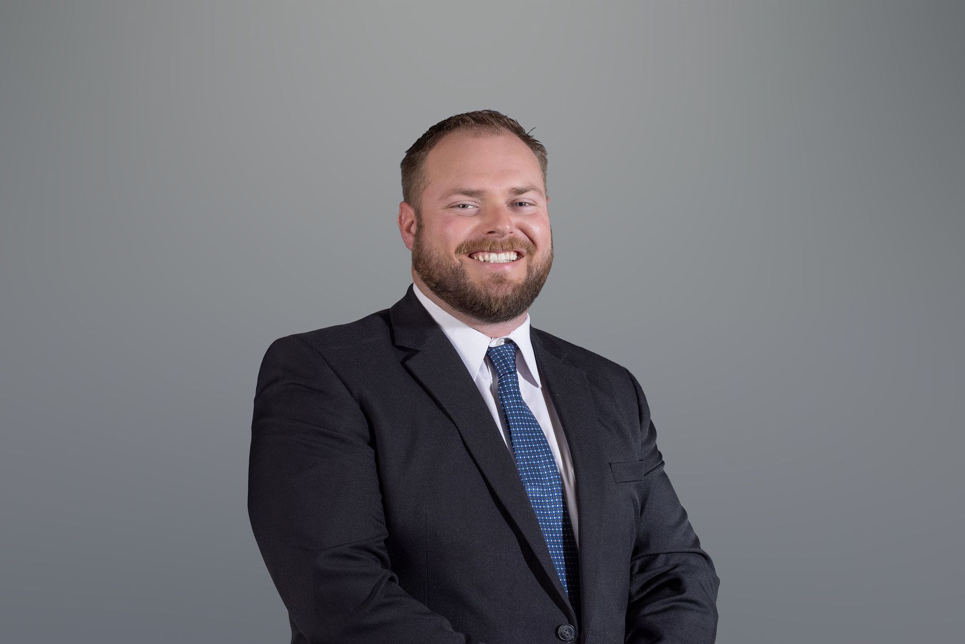 Man in dark suit and blue tie smiling against a gray background