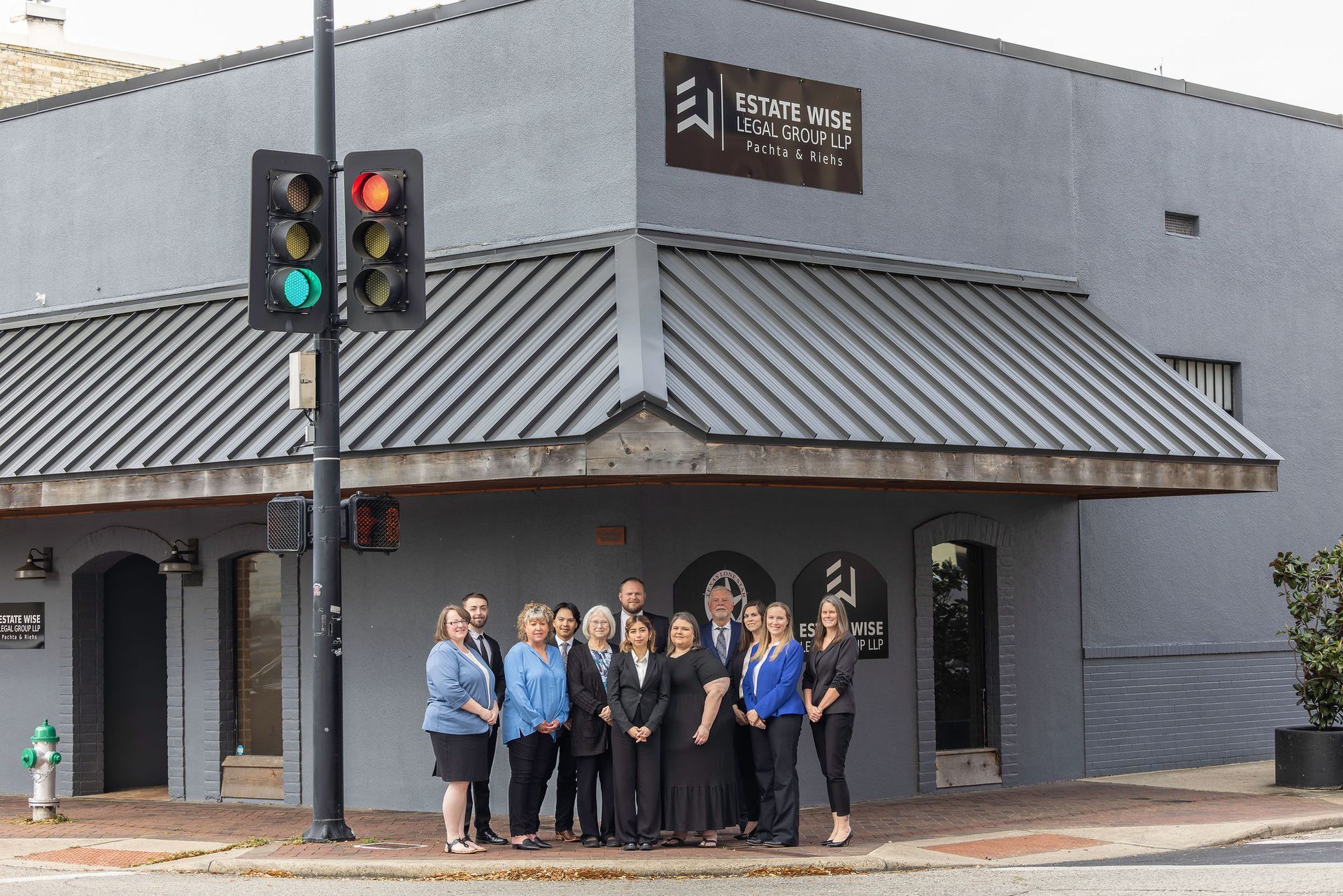 Group posing outside a gray building at a street corner, near a traffic light.