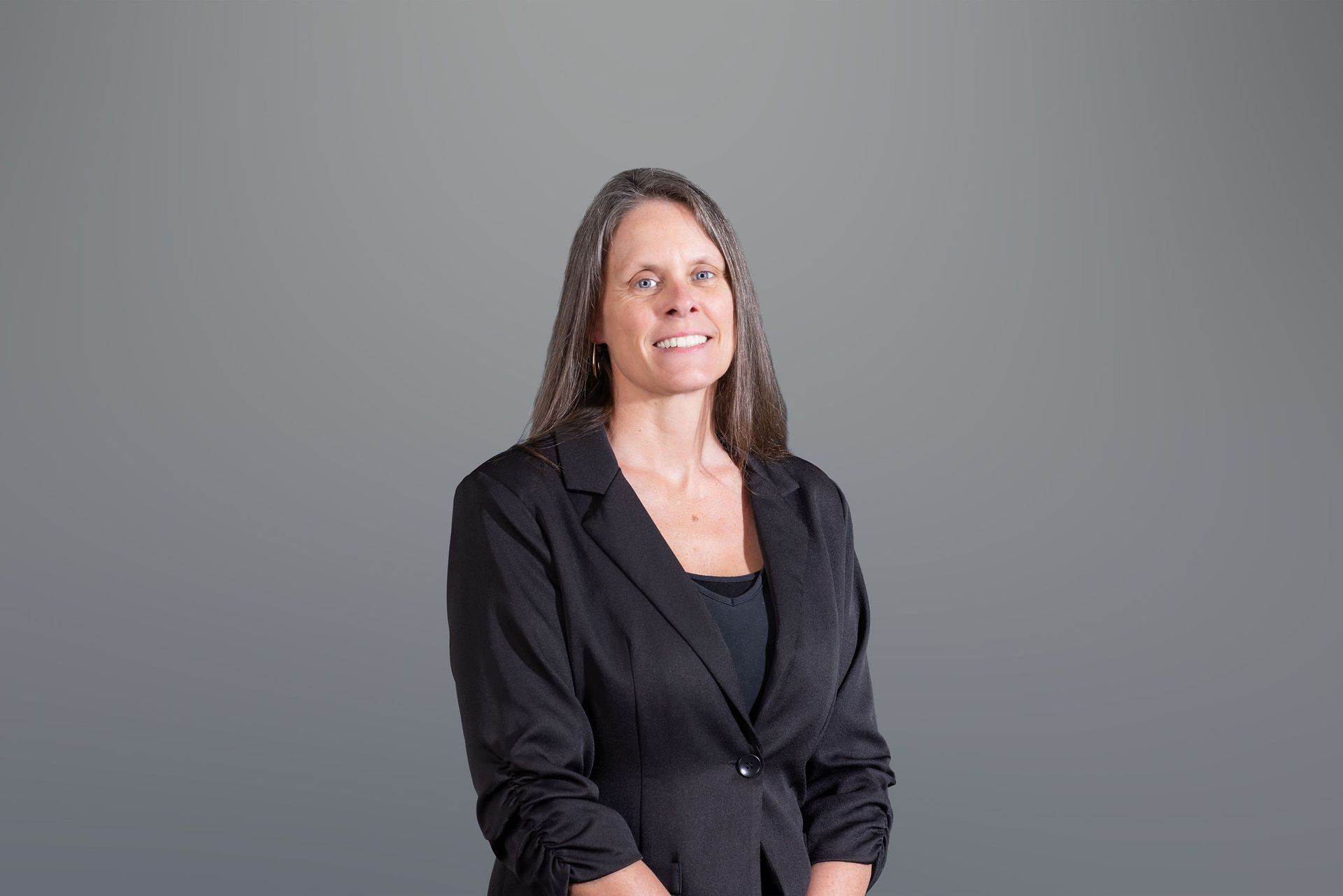 Woman in a black blazer smiling against a plain gray background