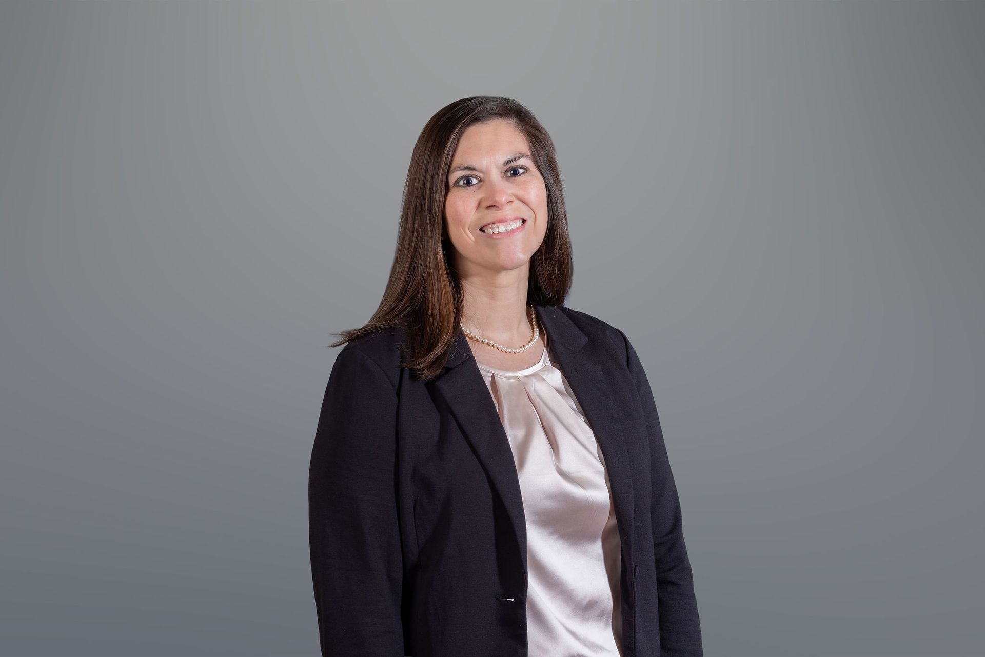 Professional woman in a black blazer and satin blouse smiling against a gray background