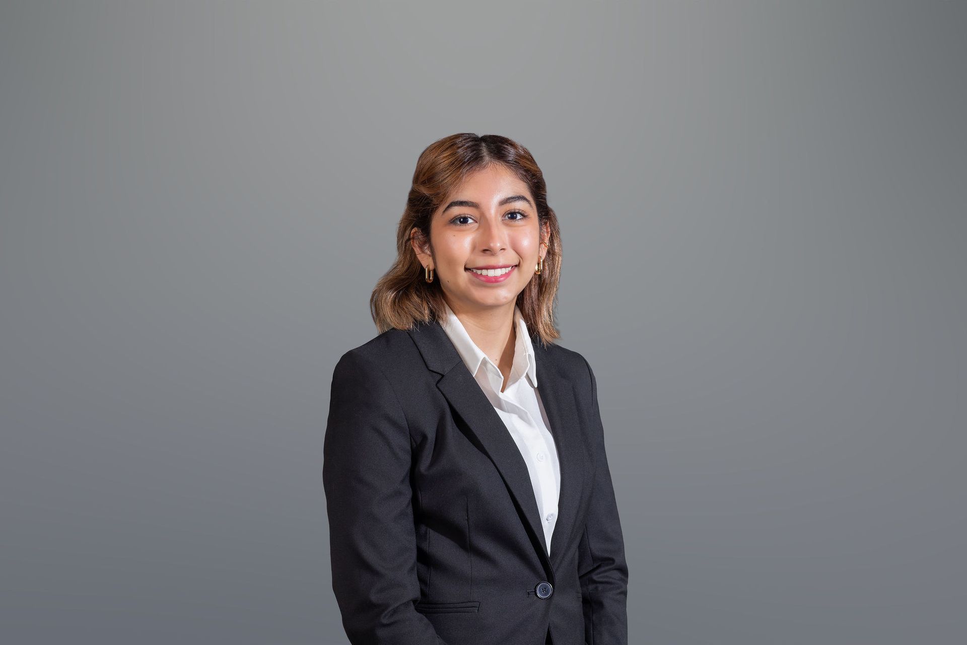 Smiling professional in a black blazer and white shirt against a gray background