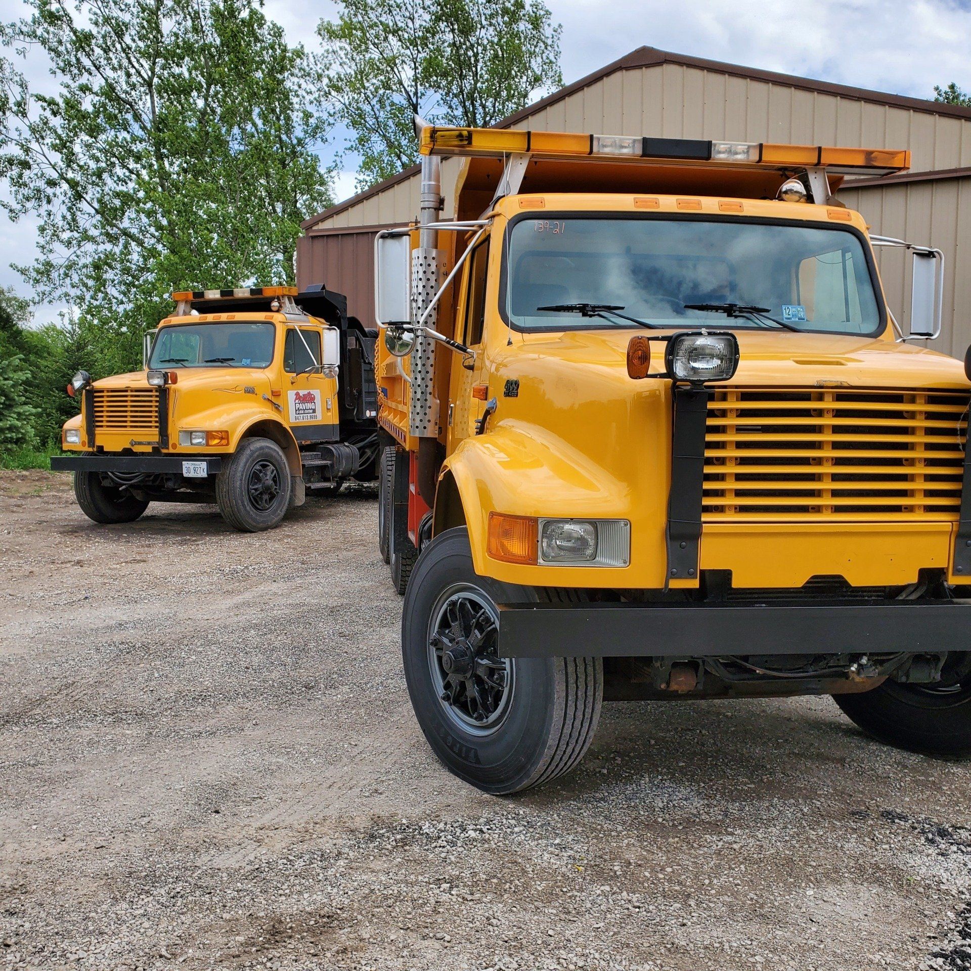Two bright yellow road maintenance trucks parked on gravel.